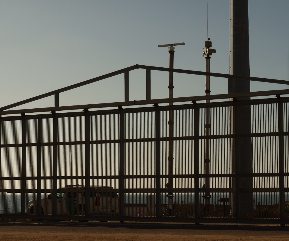 An Anduril surveillance tower at the borde fence with a Border Patrol vehicle.